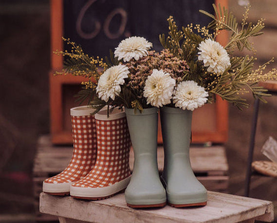 Pair of green and gingham print rain boots on a wooden stool with a bouquet of flowers and a chalkboard in the background by GRECH & CO.
