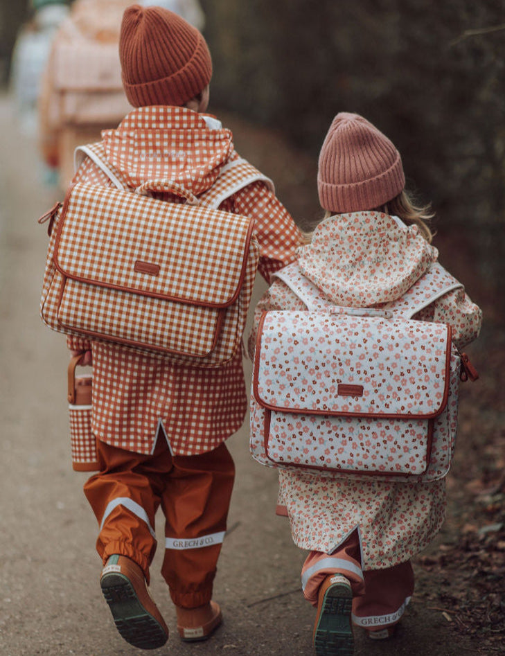 Two children walking down a path with backpacks, wearing knit hats and rain jackets by GRECH & CO.